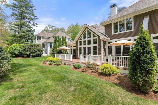 rear view of house with a chimney, a deck, and a yard