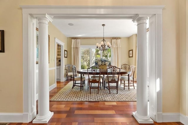 dining room featuring wood finished floors, decorative columns, baseboards, and a chandelier