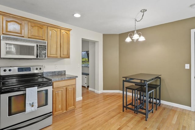 kitchen featuring baseboards, light wood-style flooring, a notable chandelier, dark countertops, and appliances with stainless steel finishes