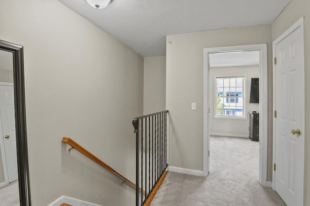 hall with baseboards, an upstairs landing, and carpet