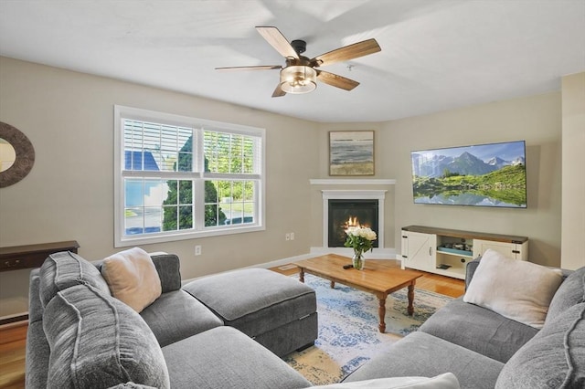 living room featuring ceiling fan, baseboards, a glass covered fireplace, and wood finished floors