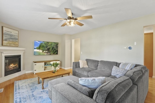 living room with wood finished floors, visible vents, baseboards, ceiling fan, and a glass covered fireplace