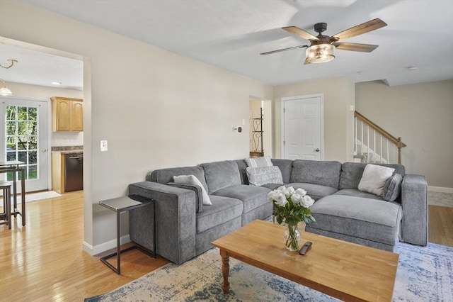 living area featuring baseboards, stairway, light wood finished floors, and ceiling fan