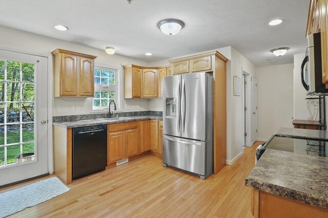 kitchen with a sink, black dishwasher, light wood-type flooring, stainless steel fridge with ice dispenser, and dark countertops