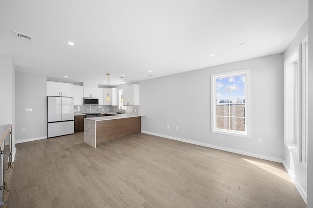 kitchen with visible vents, stainless steel microwave, light wood-type flooring, and freestanding refrigerator