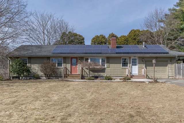 single story home featuring a chimney, a front lawn, solar panels, and an attached garage