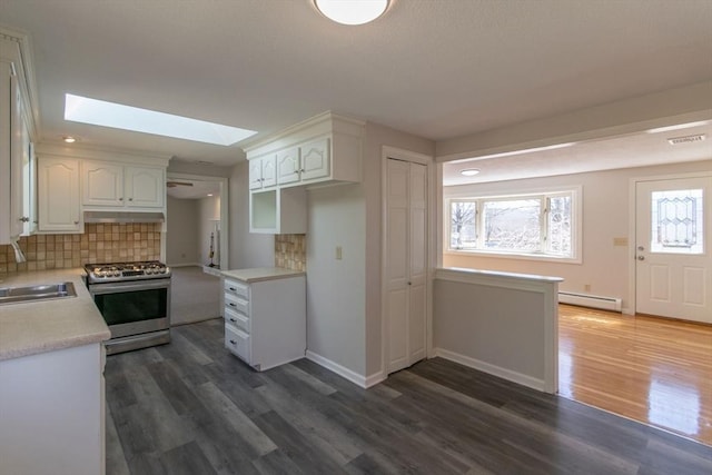 kitchen featuring gas range, light countertops, a skylight, white cabinetry, and a baseboard radiator