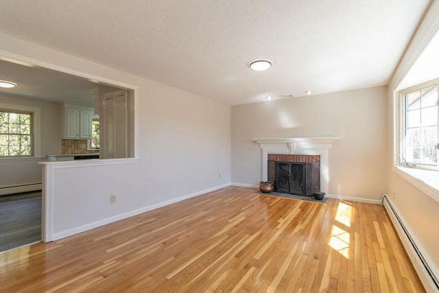 unfurnished living room featuring a baseboard heating unit, baseboards, light wood-type flooring, a fireplace, and a textured ceiling