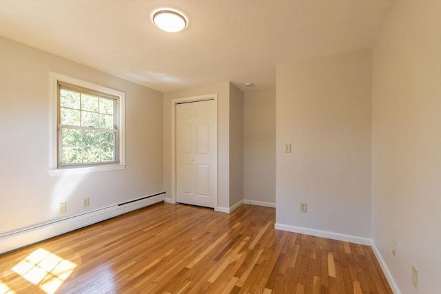 unfurnished room with a baseboard radiator, baseboards, and light wood finished floors