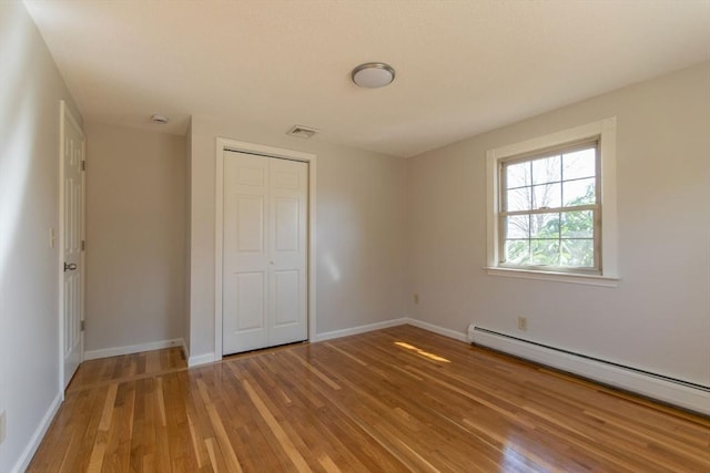 unfurnished bedroom featuring wood finished floors, visible vents, baseboards, a closet, and baseboard heating