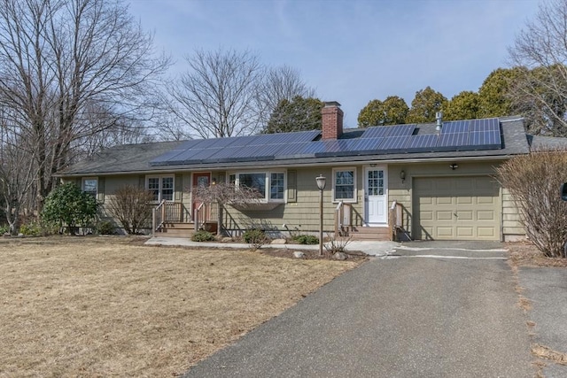 single story home featuring aphalt driveway, solar panels, an attached garage, and a chimney