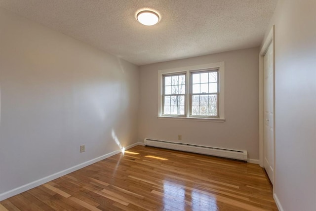 empty room featuring wood finished floors, baseboards, baseboard heating, and a textured ceiling