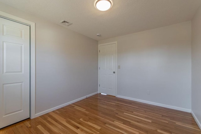 empty room with visible vents, a textured ceiling, baseboards, and wood finished floors