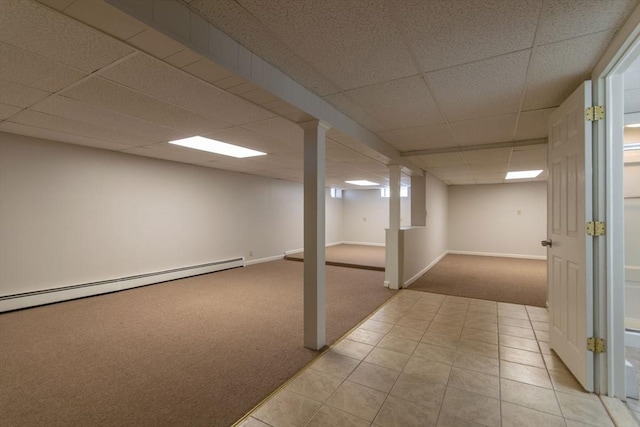 finished below grade area featuring baseboards, a drop ceiling, carpet floors, tile patterned floors, and a baseboard radiator