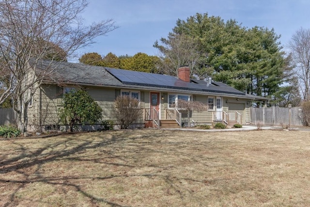 ranch-style house with roof mounted solar panels, a chimney, a front lawn, and fence