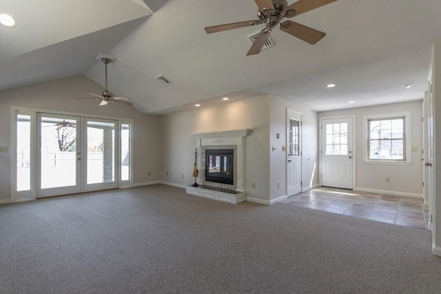 unfurnished living room with visible vents, lofted ceiling, light carpet, a tile fireplace, and a ceiling fan