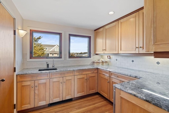 kitchen with light stone countertops, light wood-style flooring, backsplash, and a sink