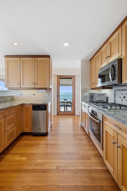 kitchen with recessed lighting, stainless steel appliances, backsplash, light stone countertops, and light wood finished floors