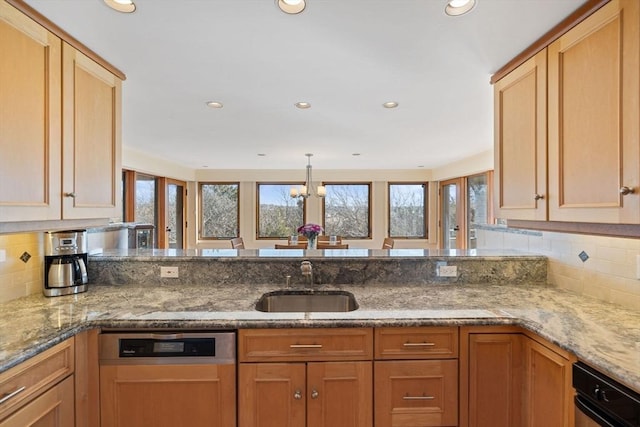 kitchen with light stone counters, a peninsula, a sink, dishwasher, and light brown cabinetry