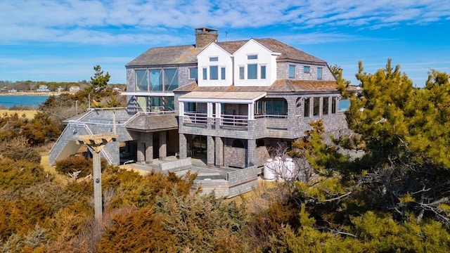 rear view of house with a water view, a balcony, and a chimney