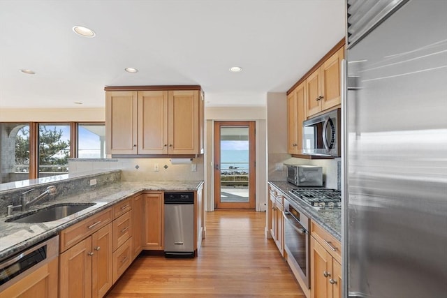 kitchen featuring backsplash, light stone countertops, stainless steel appliances, light wood-style floors, and a sink