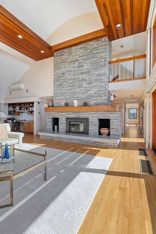 living room with a wall unit AC, wood finished floors, vaulted ceiling, a fireplace, and recessed lighting