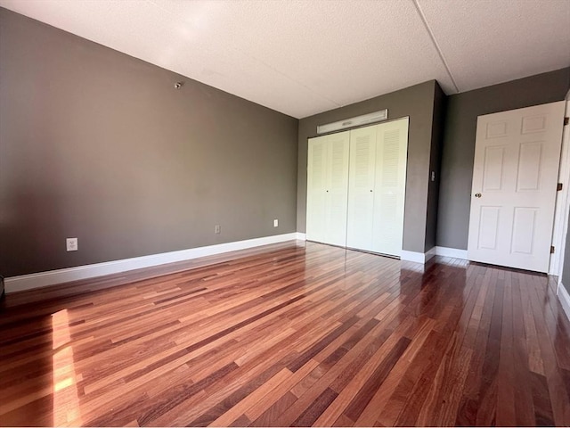 unfurnished bedroom with wood finished floors, baseboards, a closet, and a textured ceiling