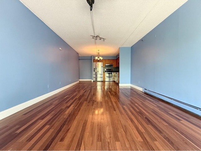 unfurnished living room featuring a chandelier, a textured ceiling, dark wood-type flooring, baseboard heating, and baseboards