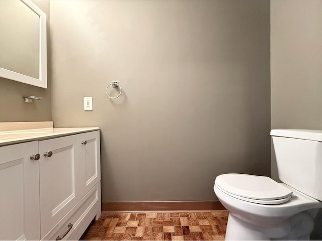 half bath with baseboards, vanity, and toilet
