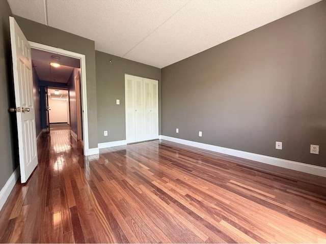 unfurnished bedroom featuring hardwood / wood-style flooring, a closet, baseboards, and a textured ceiling