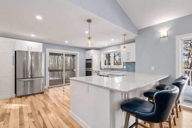 kitchen with backsplash, appliances with stainless steel finishes, white cabinets, light stone countertops, and a peninsula