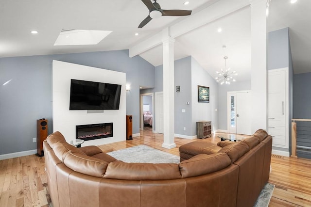 living area featuring decorative columns, light wood-style flooring, beamed ceiling, and a glass covered fireplace