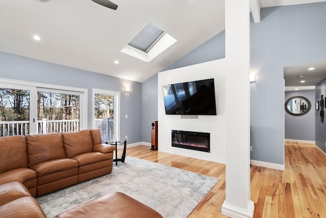 living room featuring baseboards, a glass covered fireplace, light wood-style floors, high vaulted ceiling, and recessed lighting