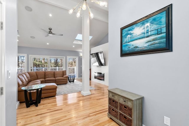 living room featuring a ceiling fan, a skylight, a glass covered fireplace, and light wood-style flooring