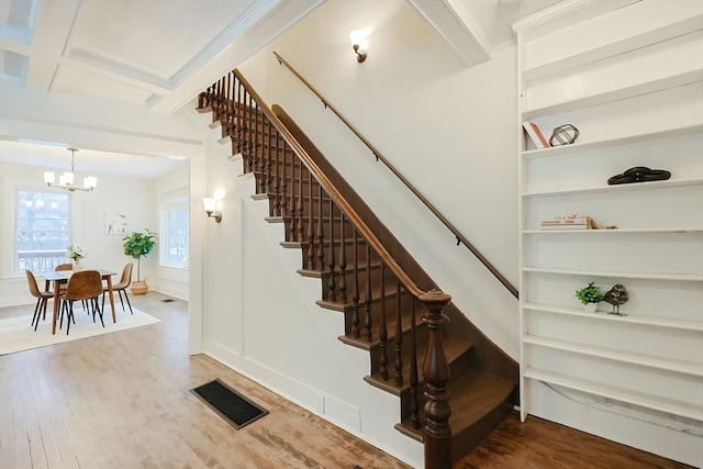 stairs featuring hardwood / wood-style flooring, a notable chandelier, coffered ceiling, and beamed ceiling