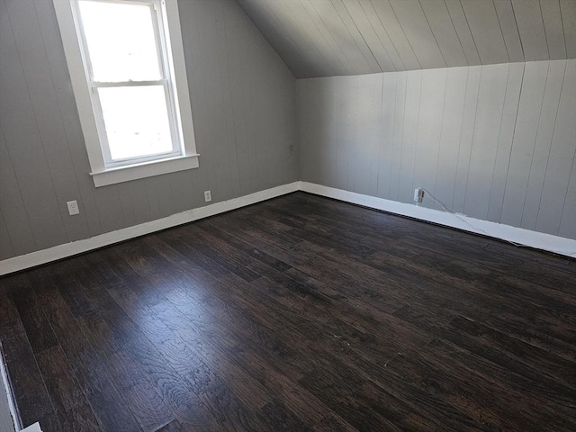 additional living space featuring dark wood finished floors, baseboards, and vaulted ceiling