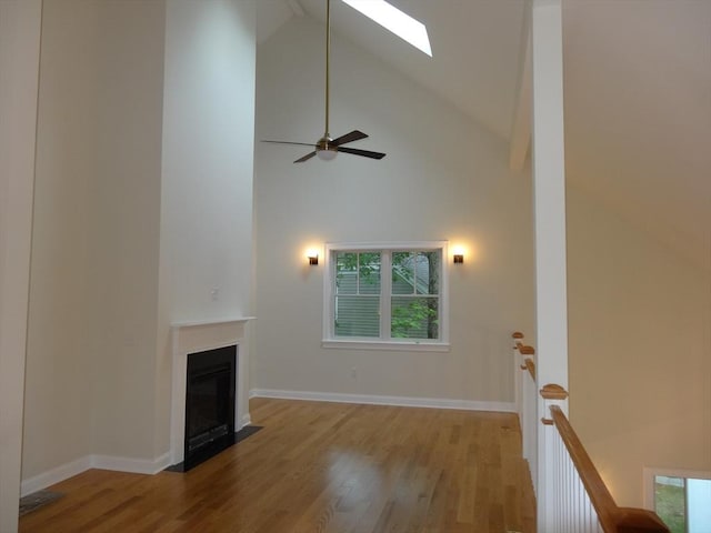 unfurnished living room with ceiling fan, high vaulted ceiling, light wood-type flooring, and a skylight