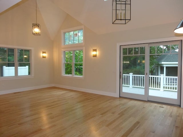 unfurnished living room featuring an inviting chandelier, high vaulted ceiling, and light hardwood / wood-style floors