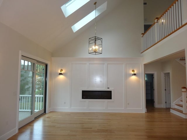 unfurnished living room with a notable chandelier, a skylight, a high ceiling, and light wood-type flooring