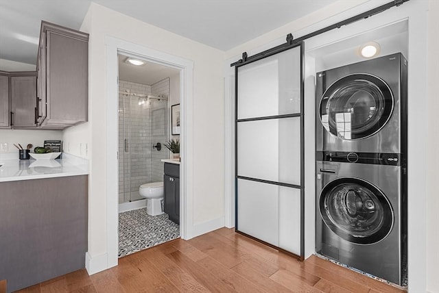 clothes washing area with a barn door, light hardwood / wood-style floors, and stacked washer / dryer