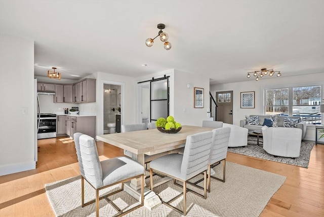 dining area with a barn door, light hardwood / wood-style flooring, and a chandelier