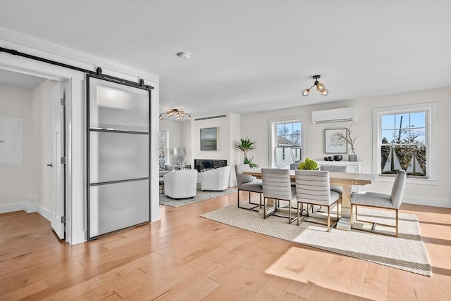 dining space with plenty of natural light, a barn door, light hardwood / wood-style flooring, and a wall mounted air conditioner