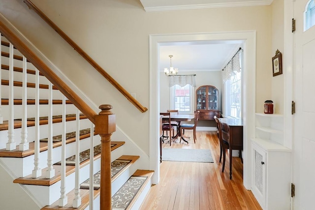 staircase with ornamental molding, hardwood / wood-style floors, and an inviting chandelier