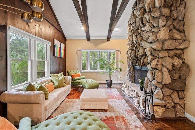 living room featuring beam ceiling, a stone fireplace, baseboards, and wood finished floors