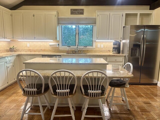 kitchen with white cabinetry, a sink, stainless steel refrigerator with ice dispenser, and a kitchen bar