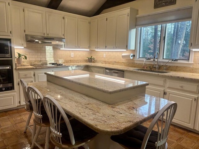 kitchen featuring white cabinets, appliances with stainless steel finishes, a center island, under cabinet range hood, and a sink