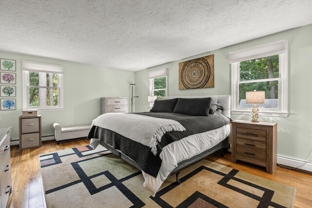 bedroom with a textured ceiling, a baseboard radiator, and wood finished floors