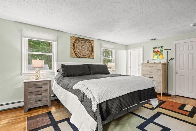 bedroom featuring a textured ceiling, baseboard heating, wood finished floors, and visible vents