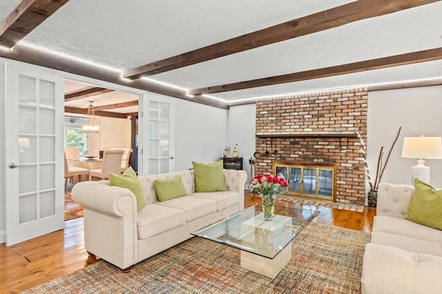 living room featuring a textured ceiling, hardwood / wood-style floors, a brick fireplace, and beam ceiling