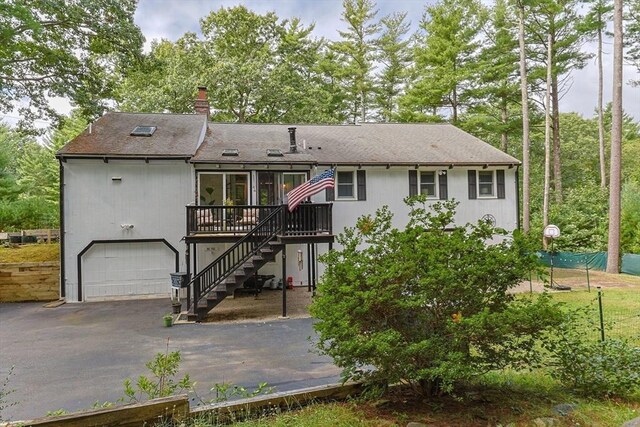 rear view of property featuring a garage, a chimney, aphalt driveway, stairs, and a wooden deck